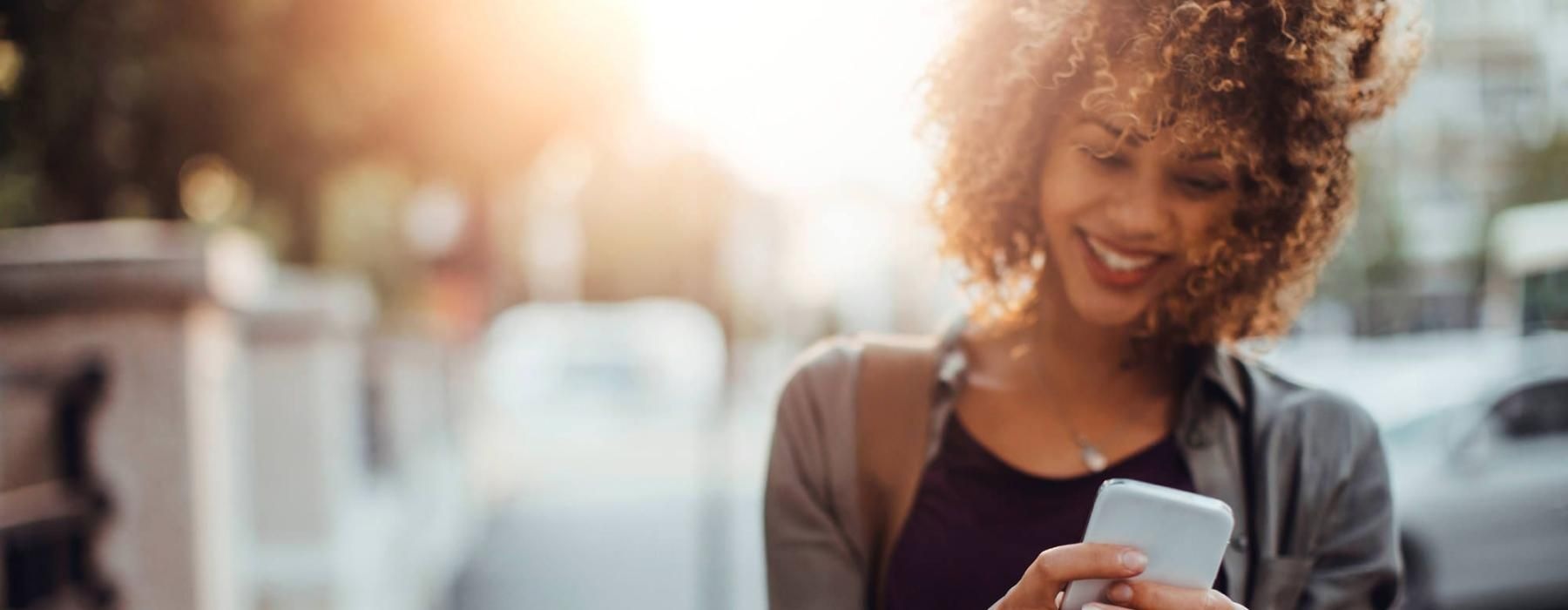 woman texts on her phone as she walks through the city