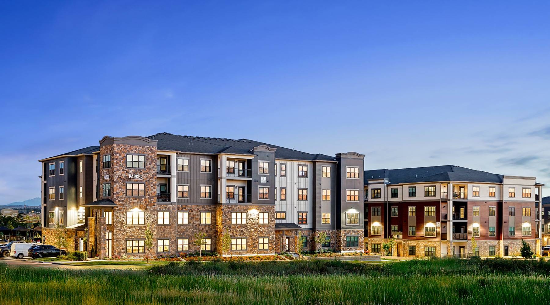 A beautiful community at the heart of all your passions twilight shot of Pine + Parker apartments lit at twilight