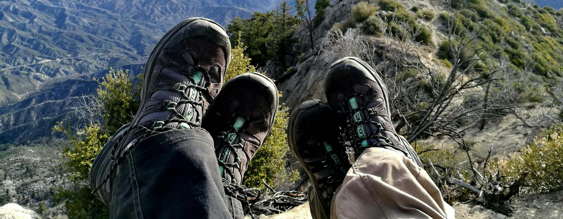 hikers' legs on a rock ledge overlooking a valley