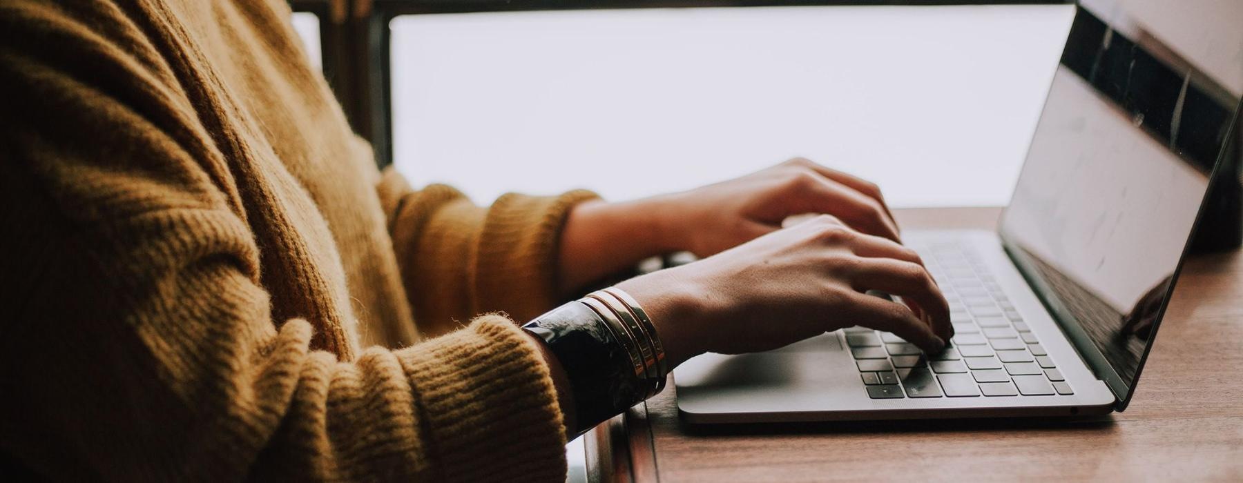 woman types on her laptop near large window